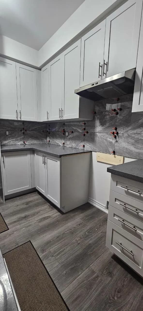 Grey large-format kitchen backsplash tile being installed between white cabinets